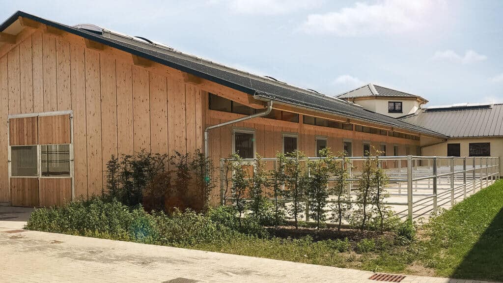 Pferdestall mit Paddocks von aussen in der Sonne
