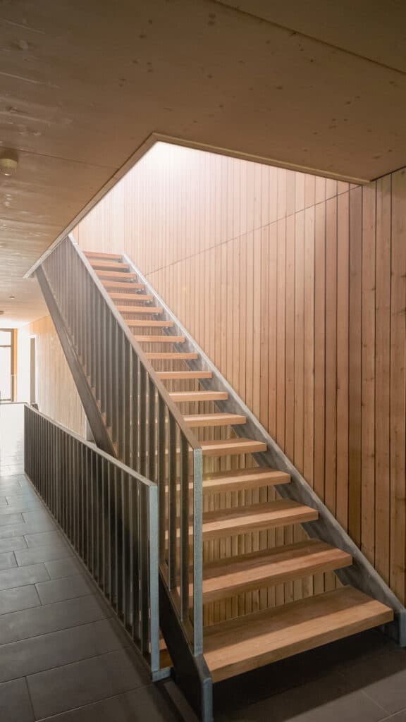 Treppe in Mehrfamilienhaus mit Holzstufen und Holzverkleidung an Wand und Decke