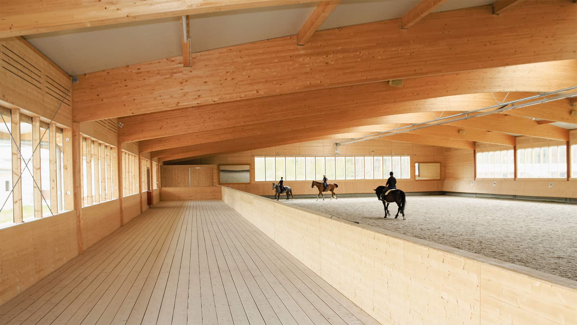 Reithalle in Holzbauweise mit drei Reiterinnen auf der Reitfläche