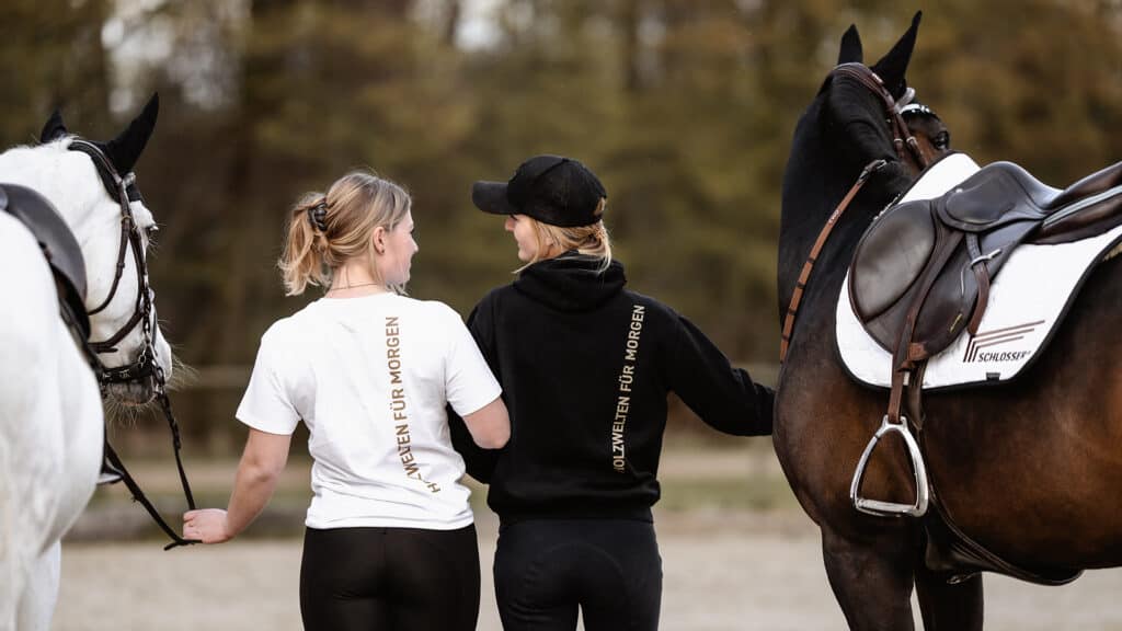 Zwei Reiterinnen in SCHLOSSER Shirt und Hoody halten ihre Pferde fest